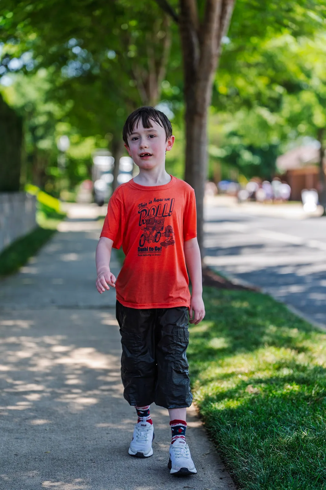 Cody in his orange shirt walking down a tree-lined path at the festival