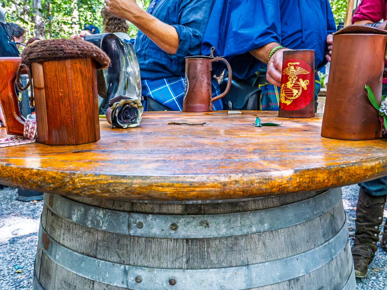 Pewter and leather drinking mugs lined up on a barrel table